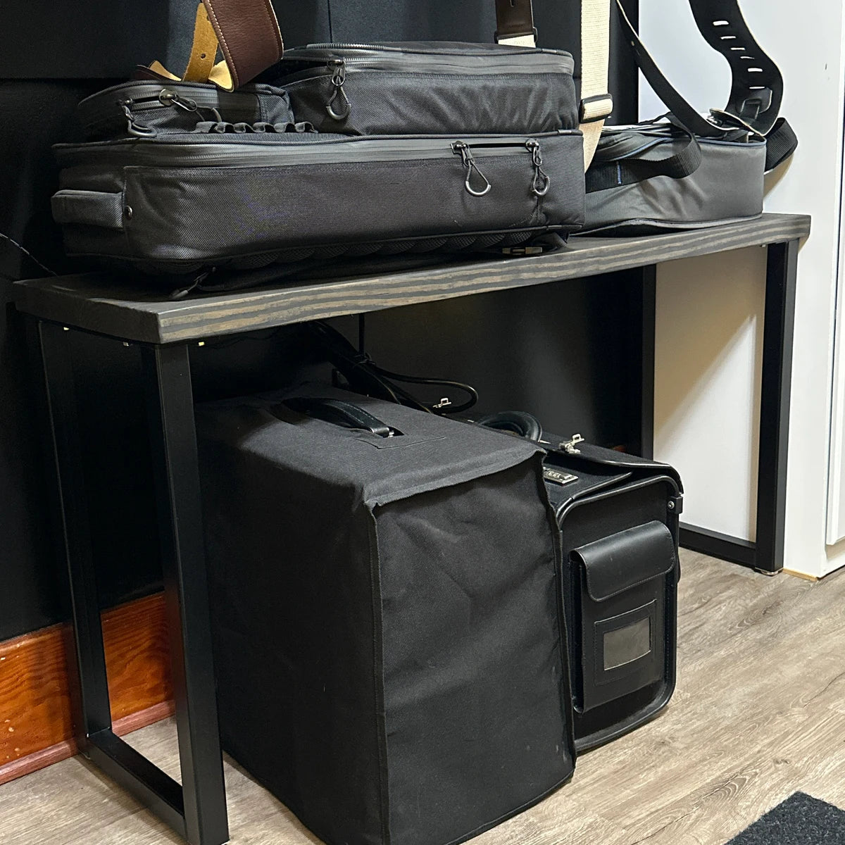 Black bags on a wooden shelf with a white wall in the background