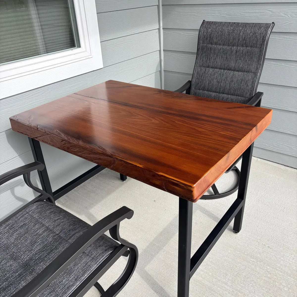 Wooden table with black metal legs and gray chairs on a patio.
